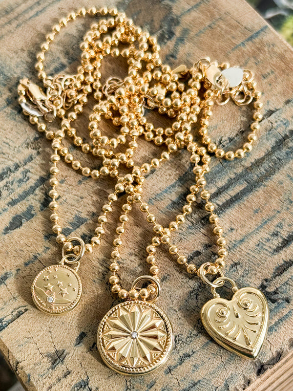 Gold beaded necklaces with star, sunburst, and heart pendants on rustic wooden surface