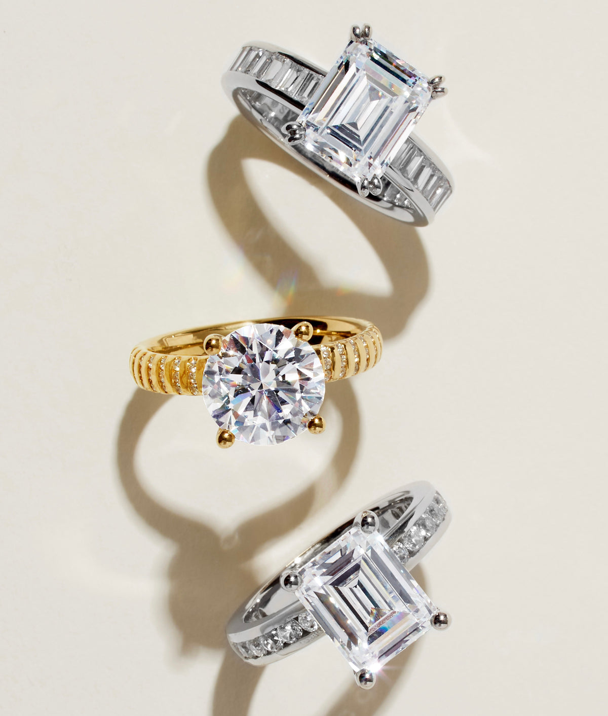 Three diamond engagement rings in gold and platinum on a cream background