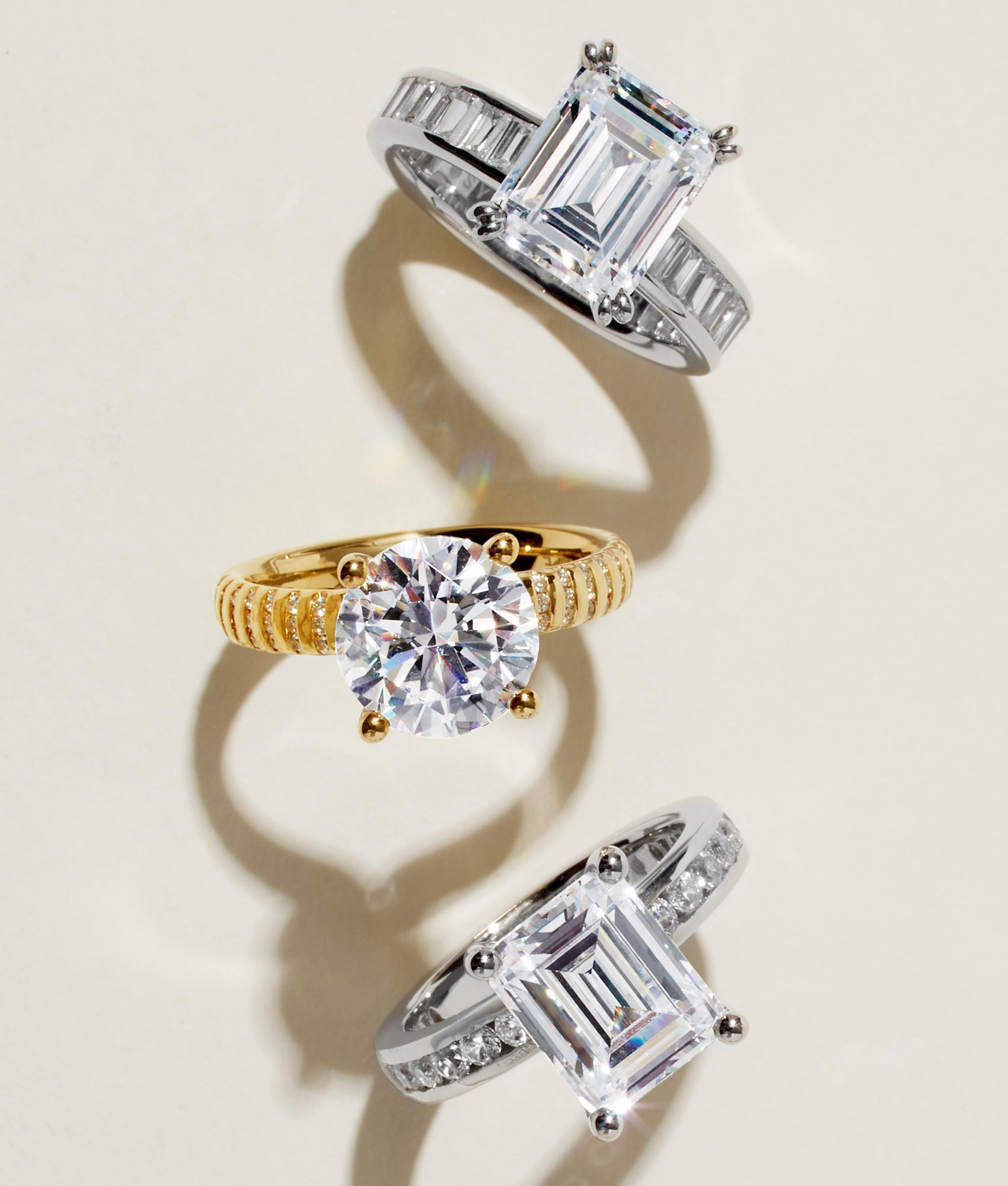 Three diamond engagement rings in gold and platinum on a cream background